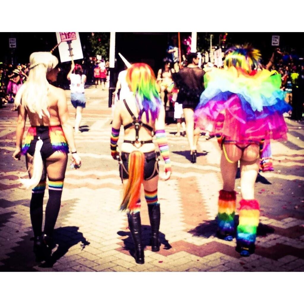 Three humans in rainbow floof and unicorn horns at Pride.