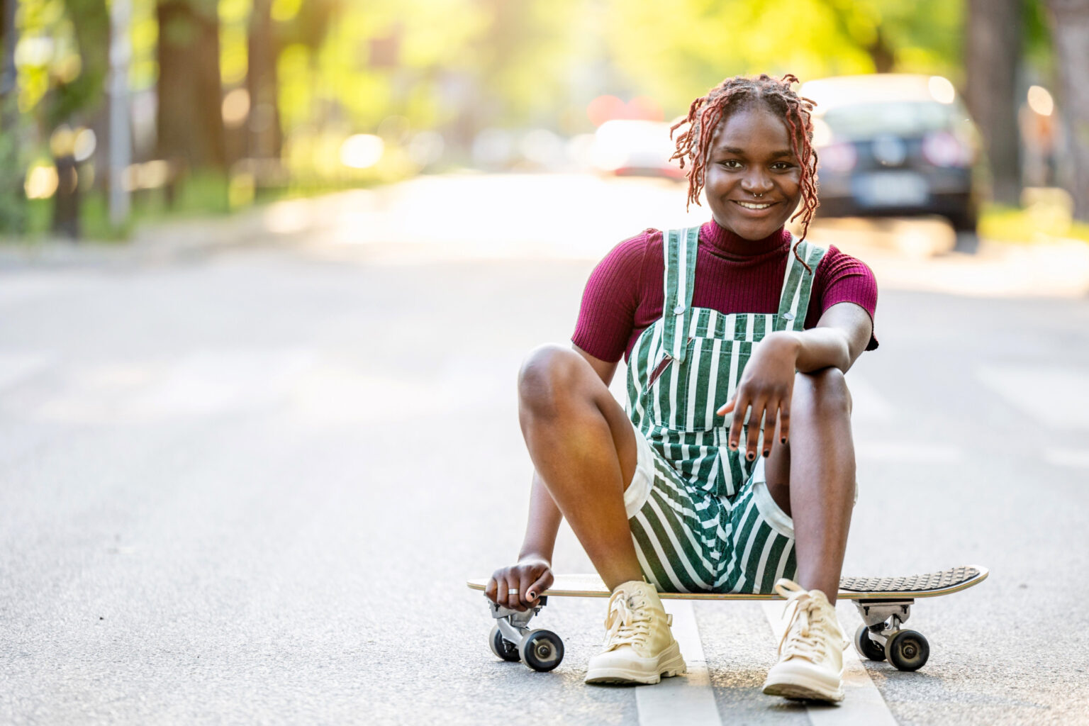 Portrait of a black non-binary person with a skateboard sitting on the street
